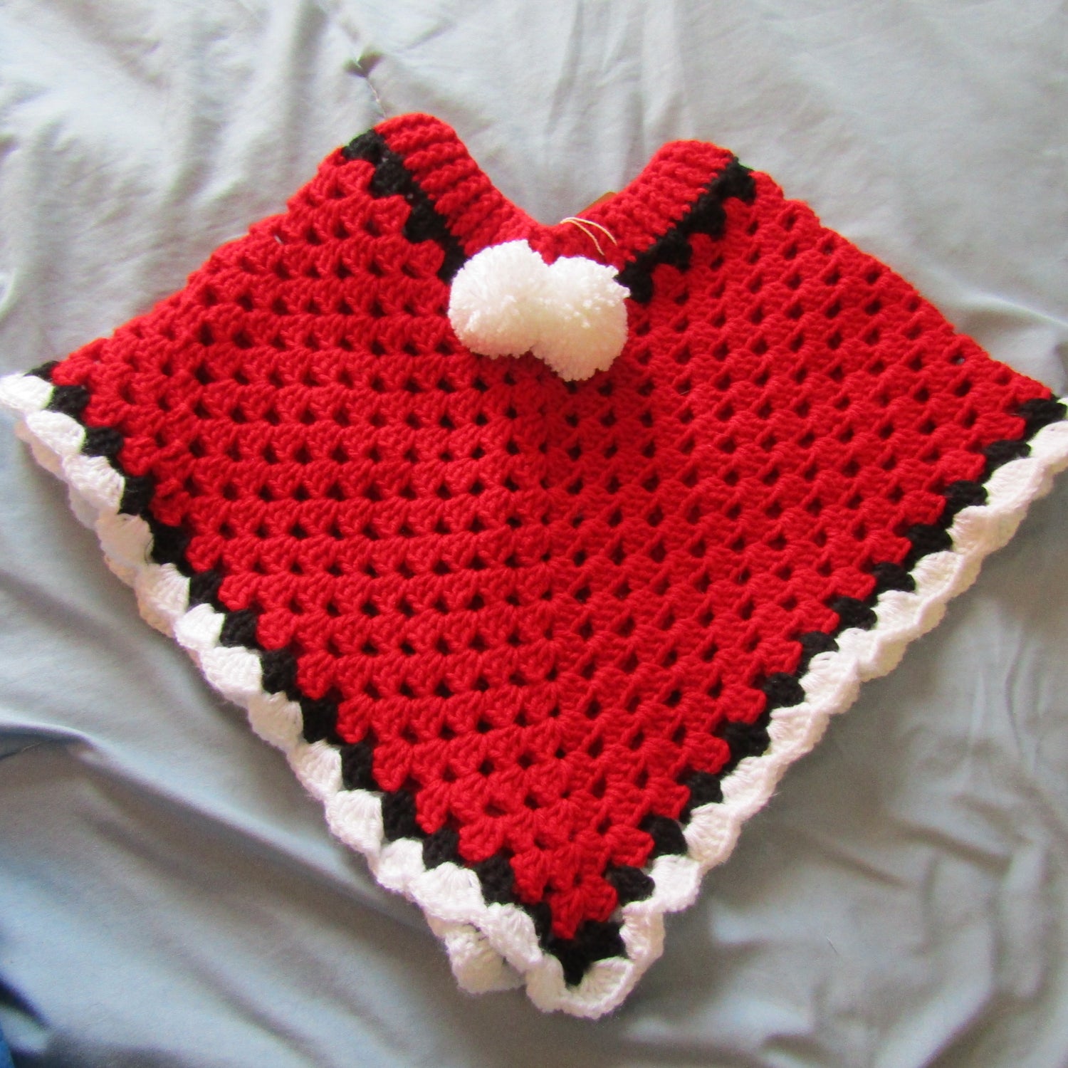 Handmade crocheted red and black poncho for kids. Has removable pom poms.